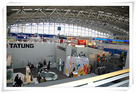 “독일 하노버 CeBIT 전시회 현장 사진. 높은 곳에서 내려다본 넓은 전시장 홀에 여러 전시 부스(‘TATUNG’ 부스 등)와 관람객들이 모여 있다.”